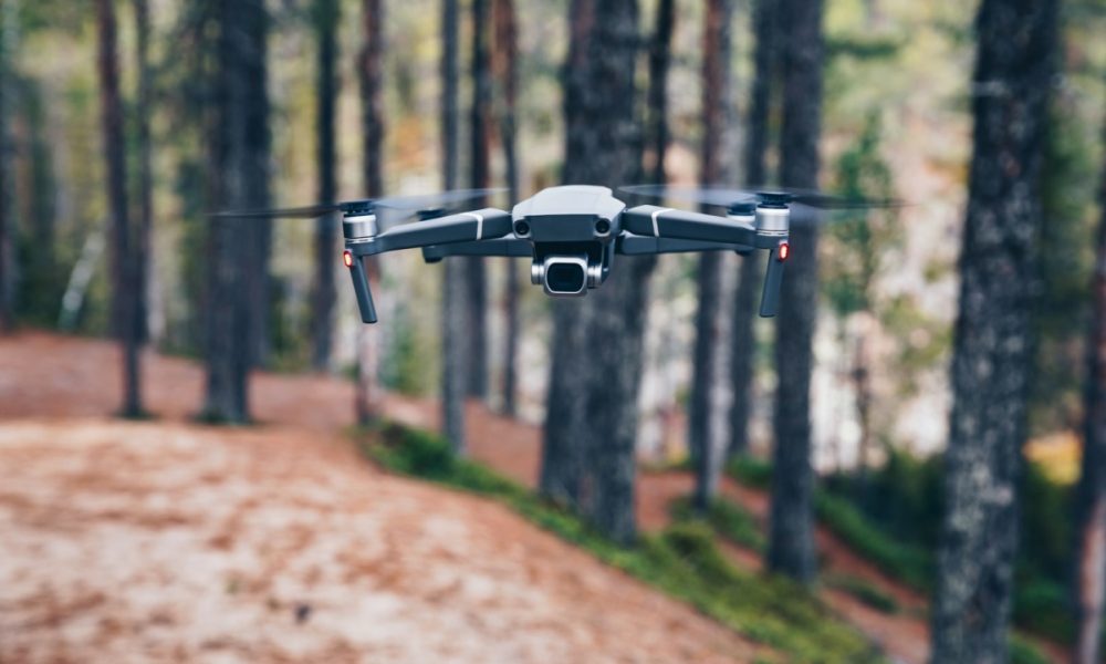 Modern Drone with camera flying in the forest.